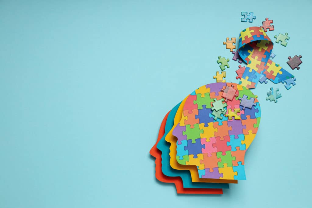 Paper human heads with colorful puzzle pieces on a light background, place for text. World autism day concept